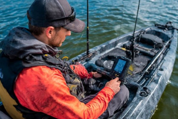 Angler adjusting portable fish finder screen brightness settings on a kayak to conserve battery power while fishing