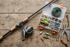 Flat lay of affordable rugged fishing gear on a weathered wooden table.